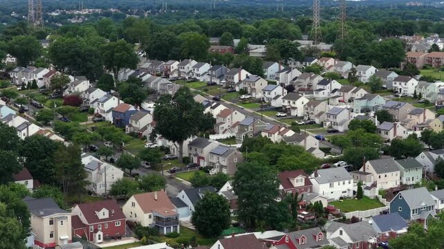 Colorful two-story American houses with rooftop solar panels line grid of quiet suburban streets, dense green tree canopy shades driveways and many parked cars below. Aerial drone wide shotAmerican su