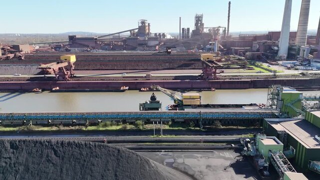 Drone flies parallel to huge coal piles unloading cranes and neatly formed raw material rows