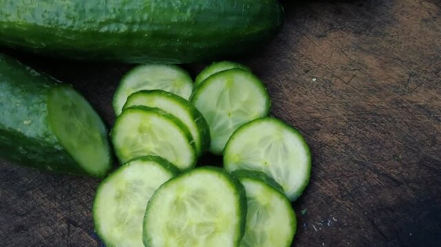 Fresh organic green cucumbers whole and sliced on rustic wooden cutting board close-up