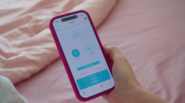 Woman records infant feeding in smartphone while baby remains close in her arms. Digital note turns recent care into useful routine, helping track timing without losing physical connection.