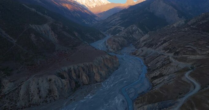 Annapurna Circuit, Manang Nepal, drone shot of the Marsyangdi River winding through rugged mountain terrain, revealing Tilicho peak in the background
