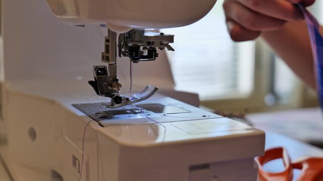 Close-up of a tailor's hands using a modern sewing machine to stitch fabric.