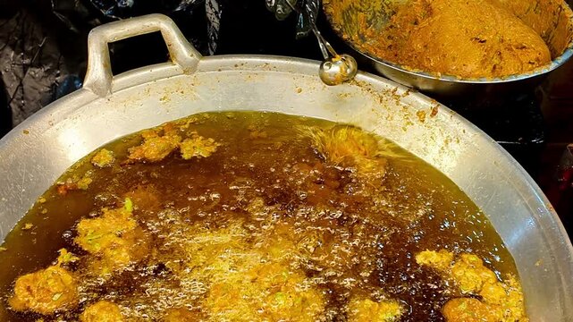Street food vendor dropping seasoned meatball mixture into a large wok filled with hot oil for deep frying at a Thai night market. Close-up of authentic Asian street food preparation with bubbling oil