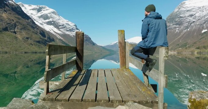 Drone Passes Man Overlooking Mirrored Lovatnet from Wooden Pier