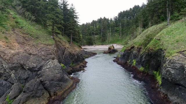 A cinematic drone shot, fly's low into Deadman's Cove, a hidden beach surrounded by rugged cliffs at Cape Disappointment, located where the Columbia River meets the Pacific Ocean in Washington.