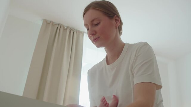 Mother provides newborn with careful hygiene care on changing table. Soft movements protect sensitive skin and keep baby comfortable, showing practical tenderness within ordinary home routine.
