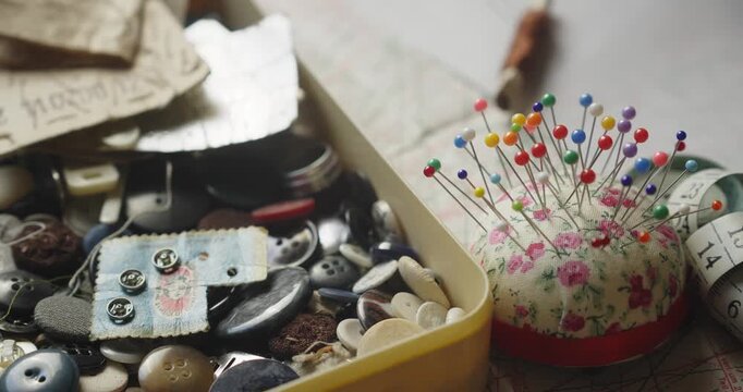 Slow pan across a dressmaking worktop revealing a measuring tape, pincushion and assorted buttons, illustrating sewing, tailoring and traditional craftsmanship.