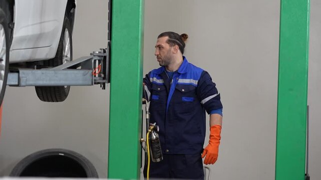 Car mechanic lift garage repair vehicle service worker inspecting raised automobile with glove in workshop uniform auto maintenance