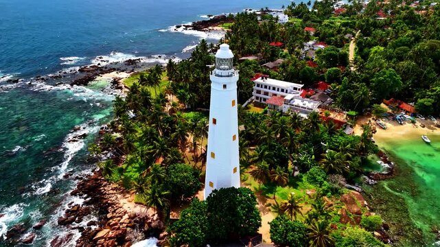 Aerial view of Barberyn Lighthouse surrounded by lush palm trees and rocky coastline in Sri Lanka.