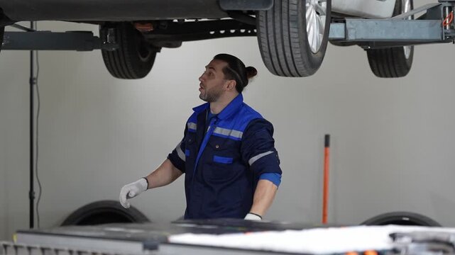 Car mechanic using lift for tire inspection and repair in garage as technician checks underside of raised vehicle during maintenance