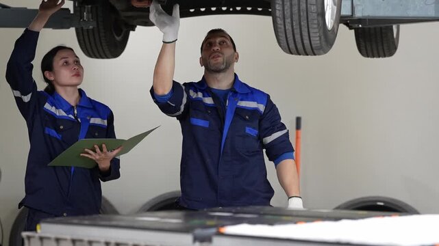Mechanic car workshop inspection tire lift service repair garage team checking vehicle undercarriage with clipboard tools maintenance