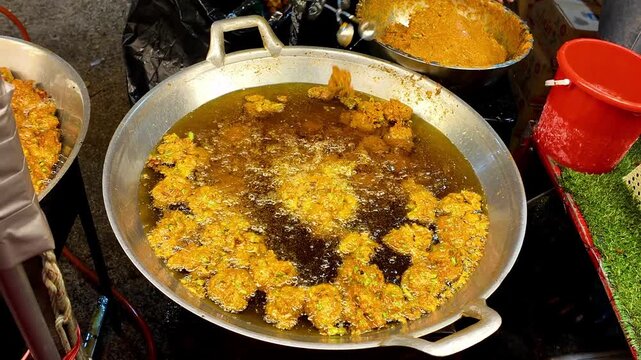 Large batch of freshly made Thai meatballs deep frying in bubbling hot oil inside a wide metal wok at a busy street food market. Authentic Asian street food cooking process with golden meatballs fryin