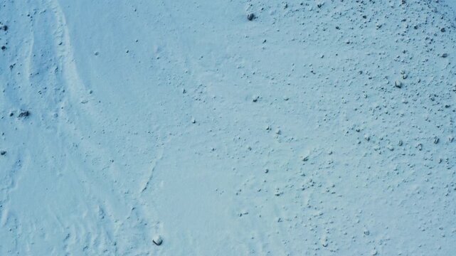 Snow-covered terrain in top-down view as drone advances and gradually slows.