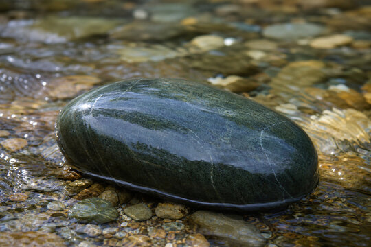 A polished soapstone rock in a clear stream with water flowing over it.