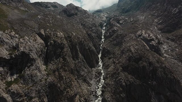 Wide view of a mountain waterfall cascading down a dark rocky gorge in Ala Archa National Park, Kyrgyzstan