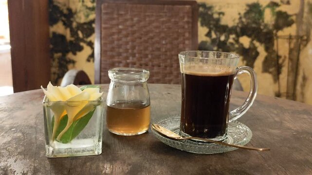 Signature Robusta black coffee from Java, Indonesia, served in a glass on a wooden table within a room featuring a classic, vintage ambiance. warm and calm atmosphere suitable for relaxation.