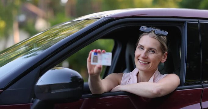 Smiling woman sitting in the car and showing her new driving license after successful driving school exam