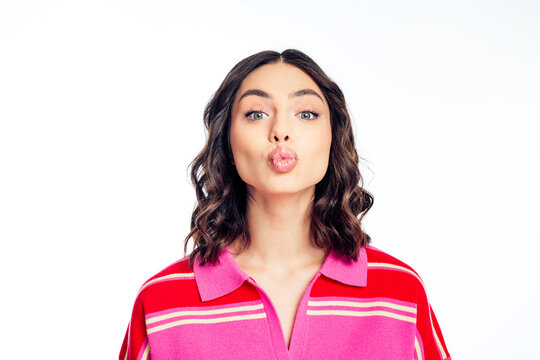 Young woman in pink striped sweater puckering her lips and making a playful kiss face to camera in a flirty studio portrait