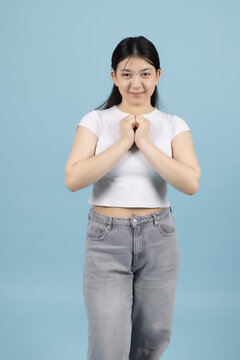 Calm young woman holding hands together in prayer position smiling in the studio