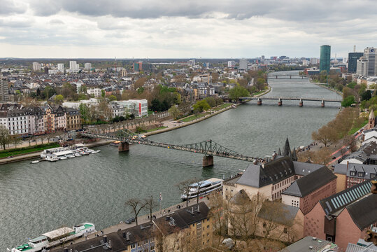 FRANKFURT AM MAIN, GERMANY &mdash; APRIL 4, 2026: Aerial view of the Main river with multiple bridges including Eiserner Steg and Holbeinsteg leading towards Westhafen Tower under a cloudy sky