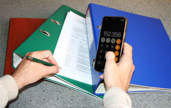 Contable con calculadora m&oacute;vil, sumar app tel&eacute;fono y apuntar en papel resultado cuenta con carpetas y archivadores 