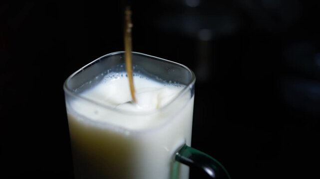 Milk being poured into a glass mug on a dark background, simple drink image with soft light and copy space