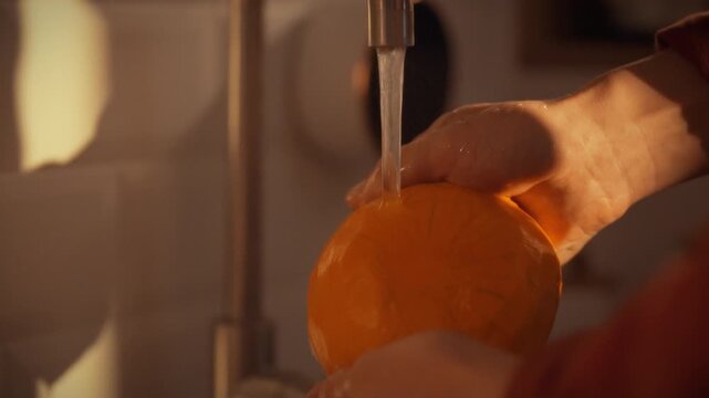 At a kitchen sink, a man's hands stream cool tap water over a peeled pumpkin, rinsing it thoroughly before cooking, highlighting the simple, fresh preparation step in everyday meal prep