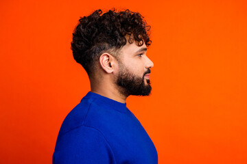 Young man profile portrait in blue sweater against bright orange background, studio side view...