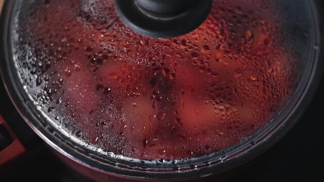 Steam builds up on the surface of a pot lid as food cooks inside. The kitchen is well-lit, showing a focus on the cooking process