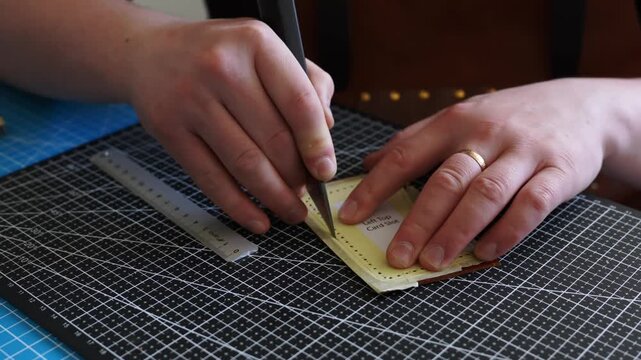 Close-up of Hands Cutting Leather with a Knife 4k video. Artisan is slicing through a raw cowhide along a paper template with a professional leatherworking blade