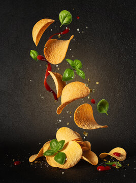 Flying potato chips with tomato sauce and fresh basil leaves on black background
