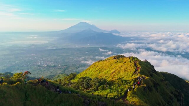 Aerial view of Mount Ungaran with hikers walking along the grassy mountain ridge above the clouds in Ungaran Barat, Central Java, Indonesia.