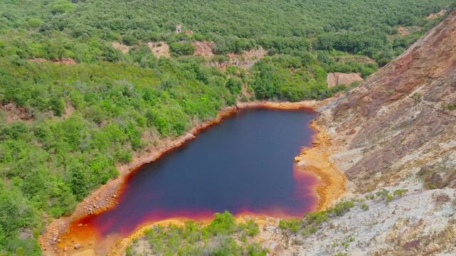 Aerial view of the red-hued Laghetto delle conche surrounded by lush green vegetation and rocky terrain in the old mining area of Rio Marina, Toscana, Italy.