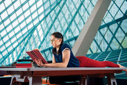 A young woman reads a book while lying on a table