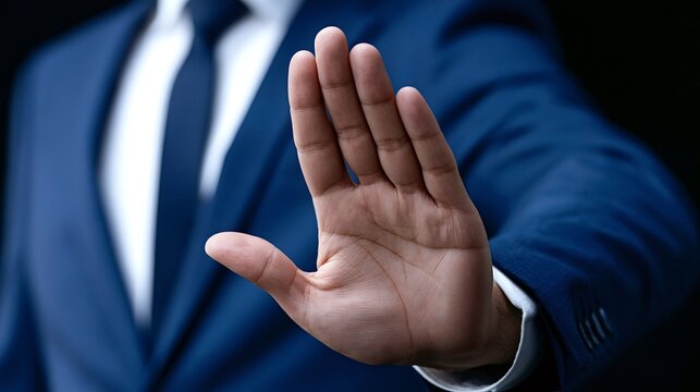 Businessman in a navy blue suit showing a stop gesture with open palm, indicating refusal, denial, or setting a boundary