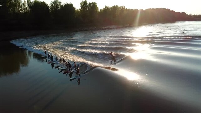 Aerial view of surfers riding the tidal bore wave on the Garonne river at sunset in Mascaret Podensac, Nouvelle-Aquitaine, France.