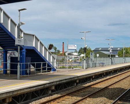 Forres railway station platform with blue metal stairs and signs under a bright sunny sky during the daytime in the Moray region of Scotland
