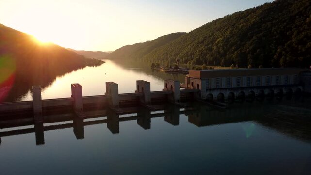 Aerial orbit of the Jochenstein hydropower plant on the river Danube against the setting sun