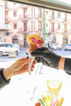 Gelataio mentre porge con un guanto nero un cono gelato ad un cliente della gelateria