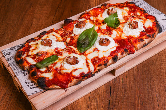 Pizza in pala croccante appena sfornata e condita con rag&ugrave; napoletano, ricotta, polpette di carne fritte, mozzarella e basilico fresco servita in una pizzeria