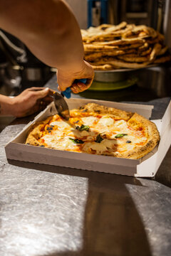 Pizzaiolo mentre taglia nel cartone da asporto una pizza margherita tradizionale napoletana con sugo di pomodoro, mozzarella e basilico