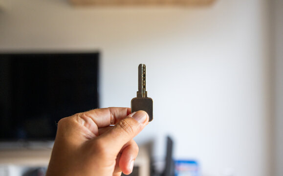 Primer plano de una mano sosteniendo una llave de seguridad vertical en un sal&oacute;n luminoso, concepto de entrega de llaves, alquiler de apartamento y nuevo hogar.