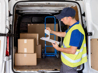 Focused man courier verifying parcels on clipboard before delivery route