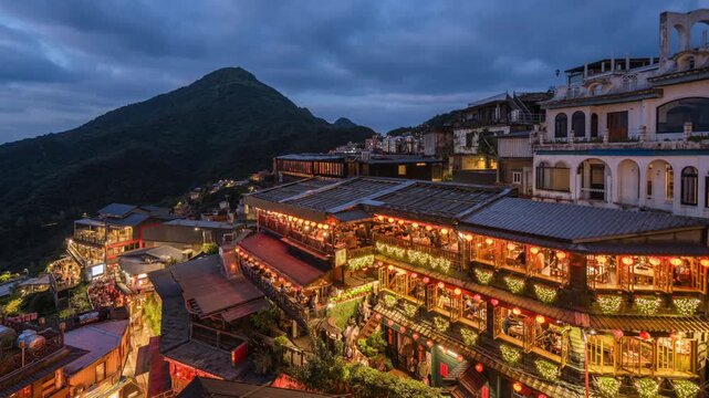 Dusk to night timelapse showing tourists visiting the famous Old Street shops and teahouses in Jiufen, New Taipei City, Taiwan, zooming out.