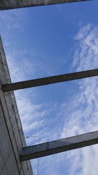 Looking up at concrete tunnel beams framing a blue sky with scattered clouds, capturing modern infrastructure, architectural geometry and urban engineering design.