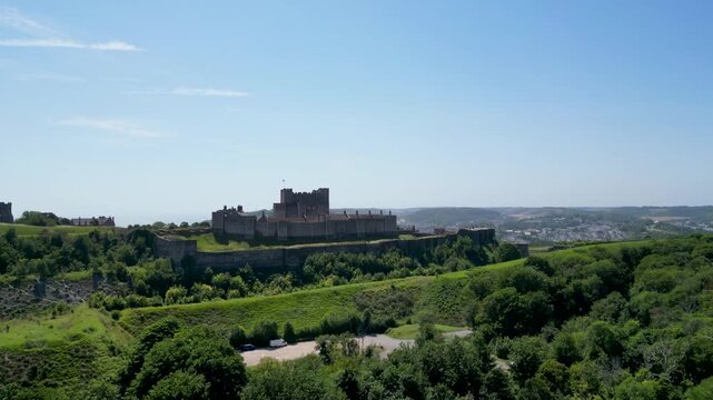 Aerial view of Dover Castle, a historic medieval fortress, set amidst lush green hills under a clear blue sky in Dover, England, United Kingdom.