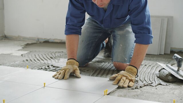 A professional construction worker kneeling on the floor while carefully installing new ceramic tiles in a modern residential home renovation