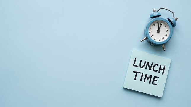 An overhead view of a blue alarm clock set for midday placed beside a square sticky note with the text lunch time written on a light blue background