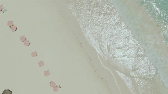 Aerial view of Pink Beach with rows of umbrellas on the sand and gentle waves washing the shore in Rock Sound, South Eleuthera, The Bahamas.