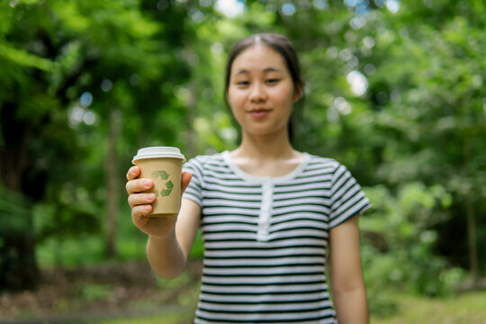 The concept of sustainable environmental practices, recycling plastic to achieve zero waste, ecology, and environmental conservation. woman holding a paper cup with a recycling symbol.